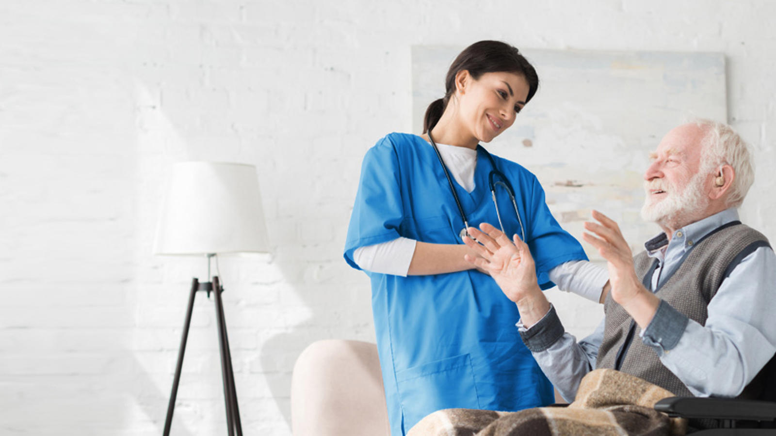 a woman in blue scrubs talking to a man in a chair