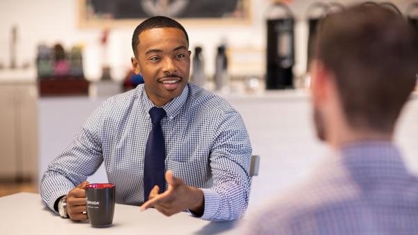a man in a blue shirt and tie talking to another man