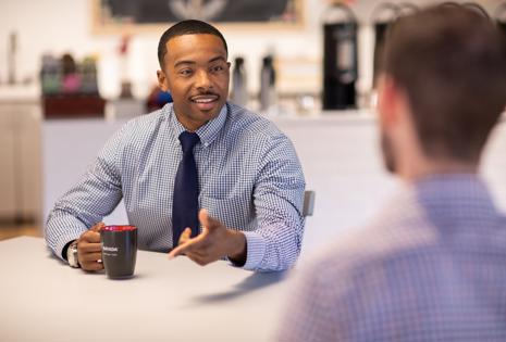 a man in a blue shirt and tie talking to another man
