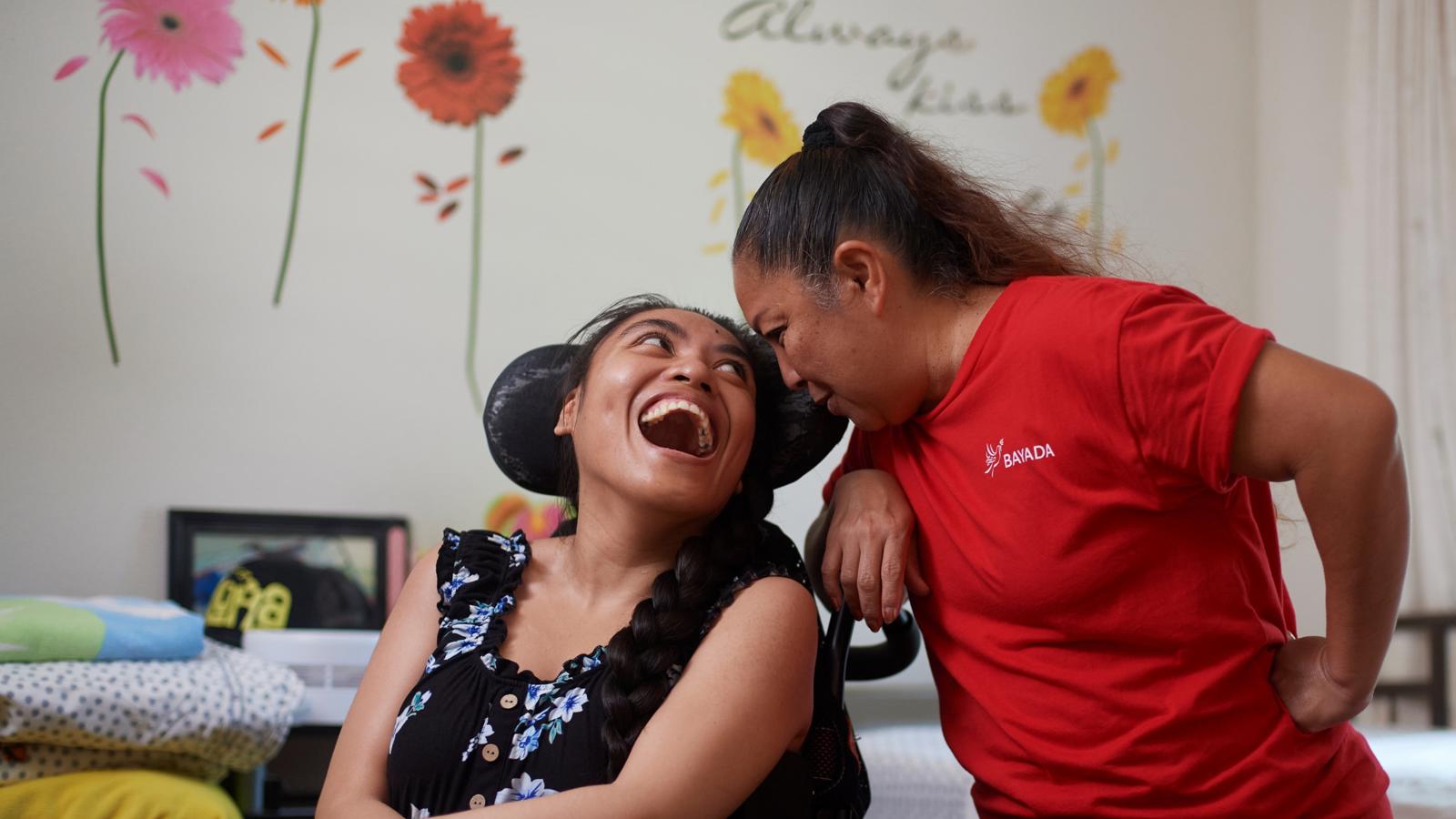 a woman in a wheelchair laughing with another woman in a room