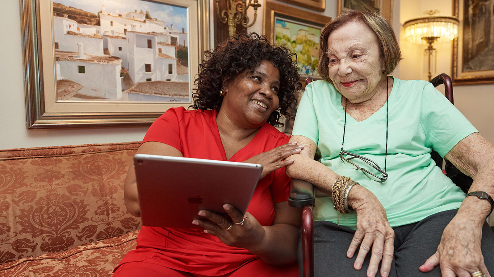 two women sitting on a couch looking at a tablet
